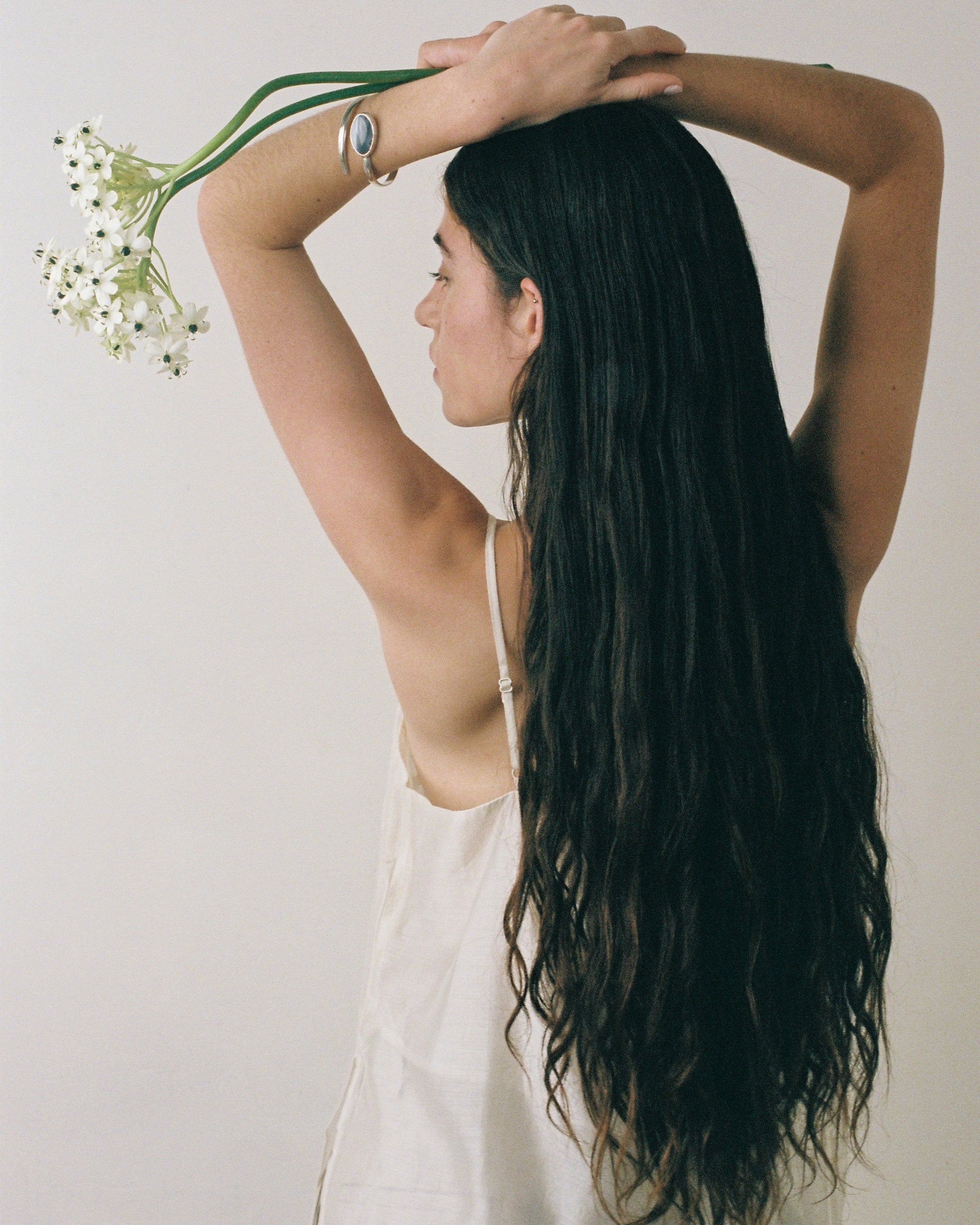 Woman with long black hair holding a small bouquet of flowers against a plain background earing sterling silver braclet with large agate